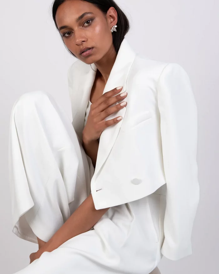 Eleganter weißer Brautblazer in Cropped-Passform, kombiniert mit fließender Hose, stilvoll inszeniert im Studio