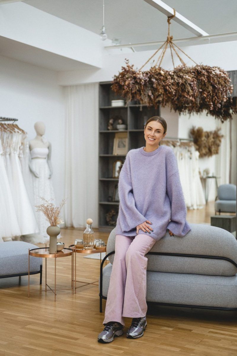 Beraterin sitzt entspannt im Showroom von Victoria Rüsche, umgeben von Brautkleidern und stilvollem Interior